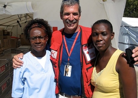 Guy standing between, with arms around, two women in Haiti