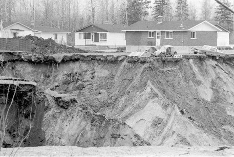 Historical black and white photo of the landslide - a rubble and mud slide with houses perched precariously at the edge.