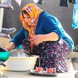 Sabah washing dishes in her makeshift shelter