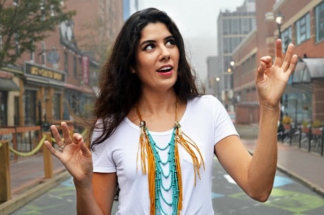 A woman with long, dark hair standing on a street with arms raised to shoulder level