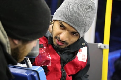 Ashwin in a Red Cross vest and grey toque talking to a man
