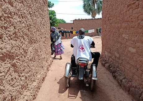 Man in a Red Cross vest driving on a motorbike on a street in Mali.