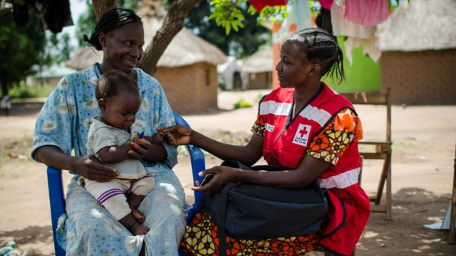  A South Sudan Red Cross personnel talks to a smiling woman holding a baby.