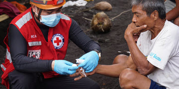 A red cross worker wearing PPE provides bandages a civilian's hand in the streets.