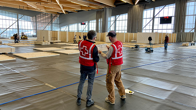 Two Canadian Red Cross vested men reviewing building plans inside an emergency resource center.