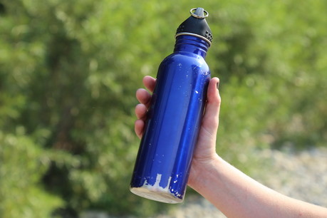 A hand holding out a blue bottle in an outdoor environment
