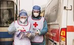 2 Red Cross Society of China volunteers wearing full protective equipment beside an emergency van.