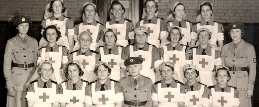 Vintage black and white photo of women in the Red Cross, most wearing aprons with large Red Cross logo