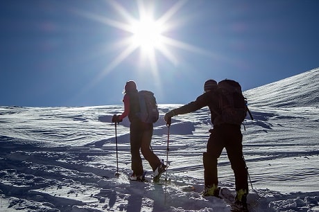 A woman and a man walk with hiking poles in the snow.