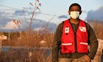 man in red cross vest with PPE standing outside looking at camera
