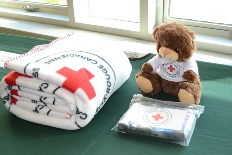 A cot with a Red Cross blanket, teddy bear and hygiene kit