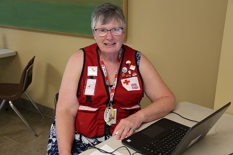 A woman sitting at a desk with a Red Cross vest on and smiling