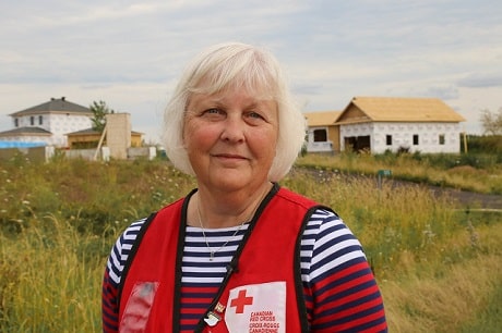 A woman in a Red Cross vest standing outside in front of homes under construction