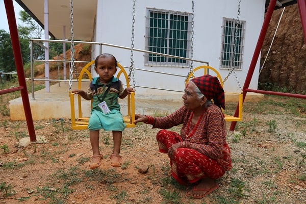 A woman and her grandchild play on a swingset