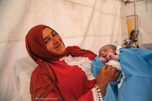 A woman holds her newborn baby in a Moroccan Red Crescent tent.