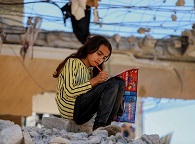 Young girl writing on a pile of rubble