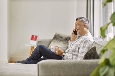 A man sitting on a couch smiling while holding a phone up to his ear