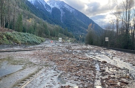 Flooded road covered in mud and debris with a large snow-topped mountain in the background