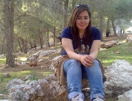A young woman sitting on a large rock with trees in the background
