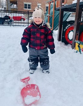 A small boy standing in front of a shovel with snow all around him.