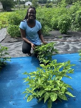Sabrina West, a volunteer, sitting in the garden with vegetables surrounding her.