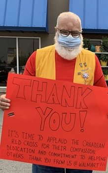 Walmart Associate Ghulam Awan standing, in mask and Walmart vest, with a poster thanking Canadian Red Cross, outside a Walmart store.