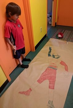 A young child standing beside a drawing of a young boy.