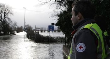 A man in a Red Cross shirt looking out at flooded roads