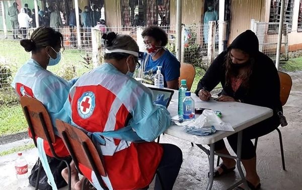 Two people in masks sitting across the table from two Red Cross members in protective equipment