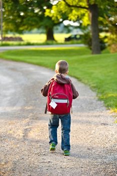 A young child walking with a backpack on.