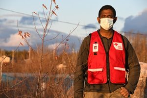 man in red cross vest wearing PPE standing outside
