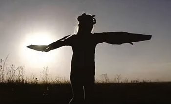 A silhouette of an Indigenous dancer with arms wide in a field