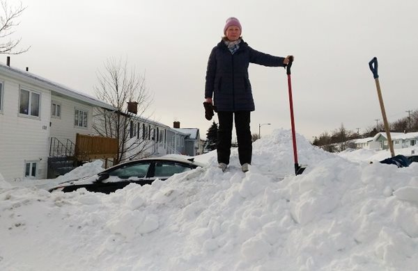 A woman standing on top of a snow pile with shovel in hand.