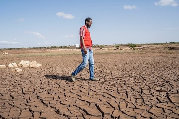 A man in a Red Cross vest walks across a dry, barren field