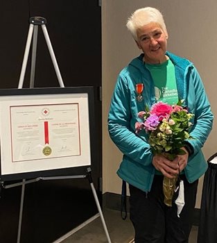 Canadian Red Cross volunteer Donna standing next to her award and holding flowers.