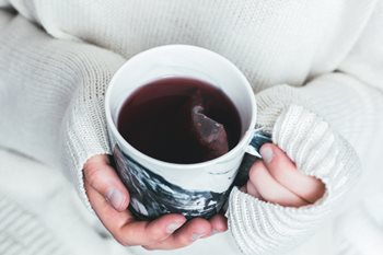 Two hands cradle a cup of red coloured tea in a black and white mug