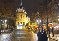 Diane standing on the streets of Paris at night with buildings and trees behind her.