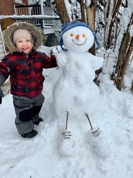 A child in winter wear standing outside by a snowman