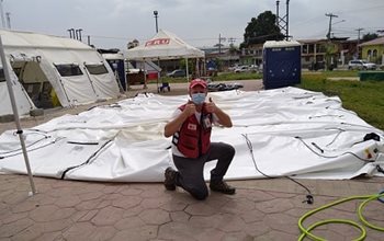 Garry in mask and red vest giving thumbs-up on top of a deflated white tent
