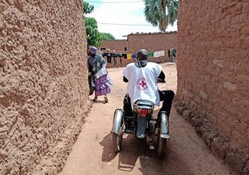 A man in a Red Cross shirt on a motorbike