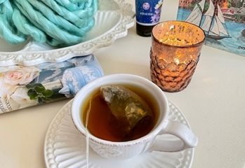 A cup of tea, candle and ball of blue yarn sit on a table