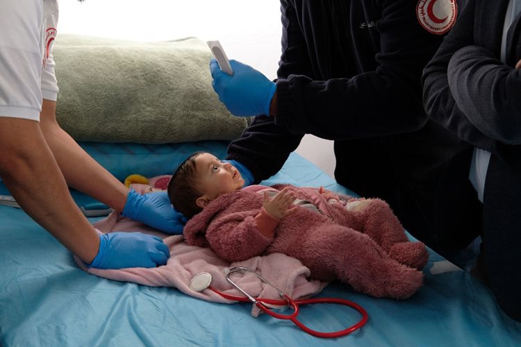 A baby receiving a medical check-up by medical staff from the Palestine Red Crescent Society.