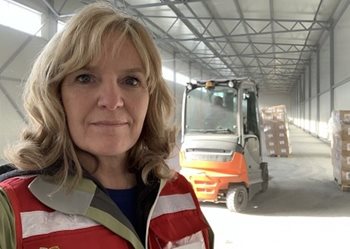 A woman in Red Cross vest standing in front of a forklift and supplies