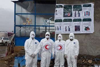 An Afghan Red Crescent mobile health team standing by a large poster on a wall.