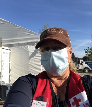 A woman in cap and mask taking a selfie with a white tent and blue sky behind her.