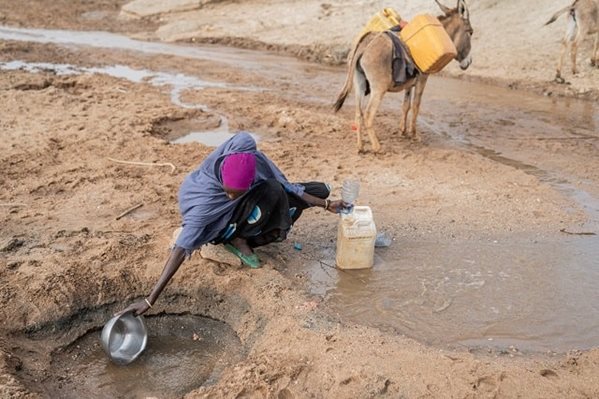 A woman bending down to scoop some water that is coming in a small trickle