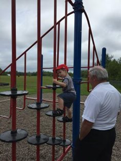 A toddler climbs on playground equipment, as a caregiver watches them