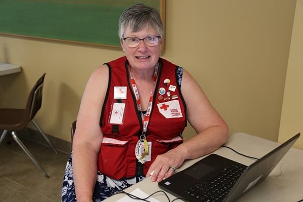 A woman in a Red Cross vest sitting at a desk, smiling