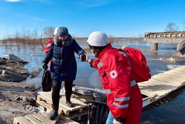 People in Red Cross jackets helping people cross over water