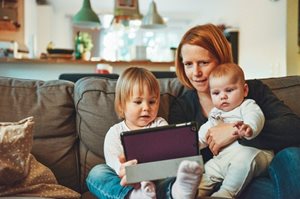 A mom sitting with a baby and a toddler looking at a tablet